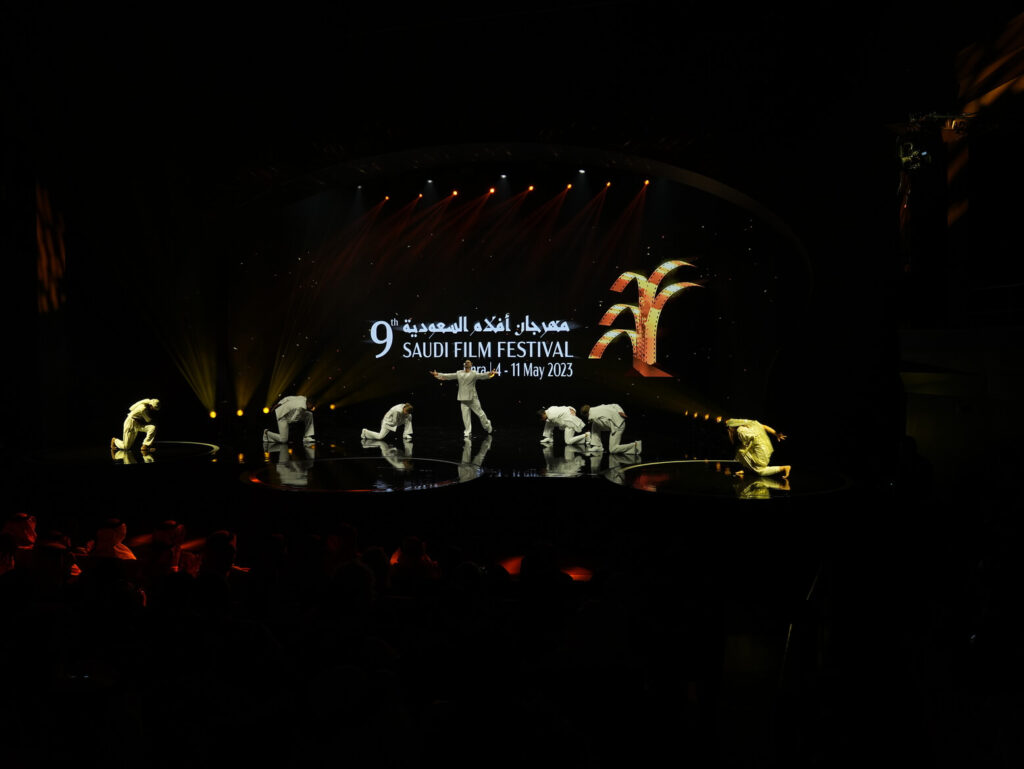 Stage performance at the Saudi Film Festival with dancers in white surrounding a central performer under dramatic lighting